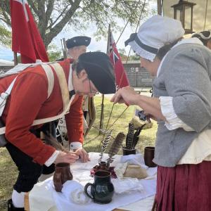The event had people dressed in historic clothing and offering traditional activities. One booth had historic clothing and jewelry that attendants could buy, while another offered food of the time, like molasses cookies. This booth, led by Cathy Potter, allowed participants to try writing with a feather and ink.
